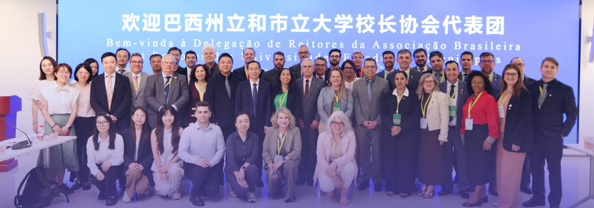45 representantes das instituições brasileira e chinesas posando para a foto em frente ao telão azul claro, com dizeres de boas-vindas à Abruem, escrito em mandarim. 
