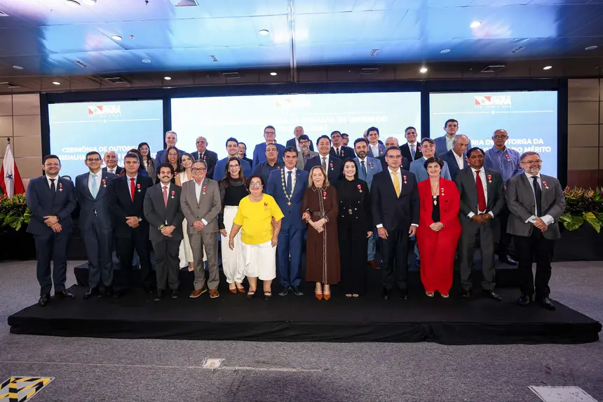 Grupo de autoridades e homenageados posa para foto oficial em um palco durante a cerimônia de outorga da Ordem do Mérito Grão-Pará. Os participantes, em sua maioria vestidos com trajes formais, exibem medalhas no peito, enquanto o governador aparece ao centro com colar cerimonial. Ao fundo, telões com a identidade visual do evento reforçam o caráter institucional e solene da ocasião.