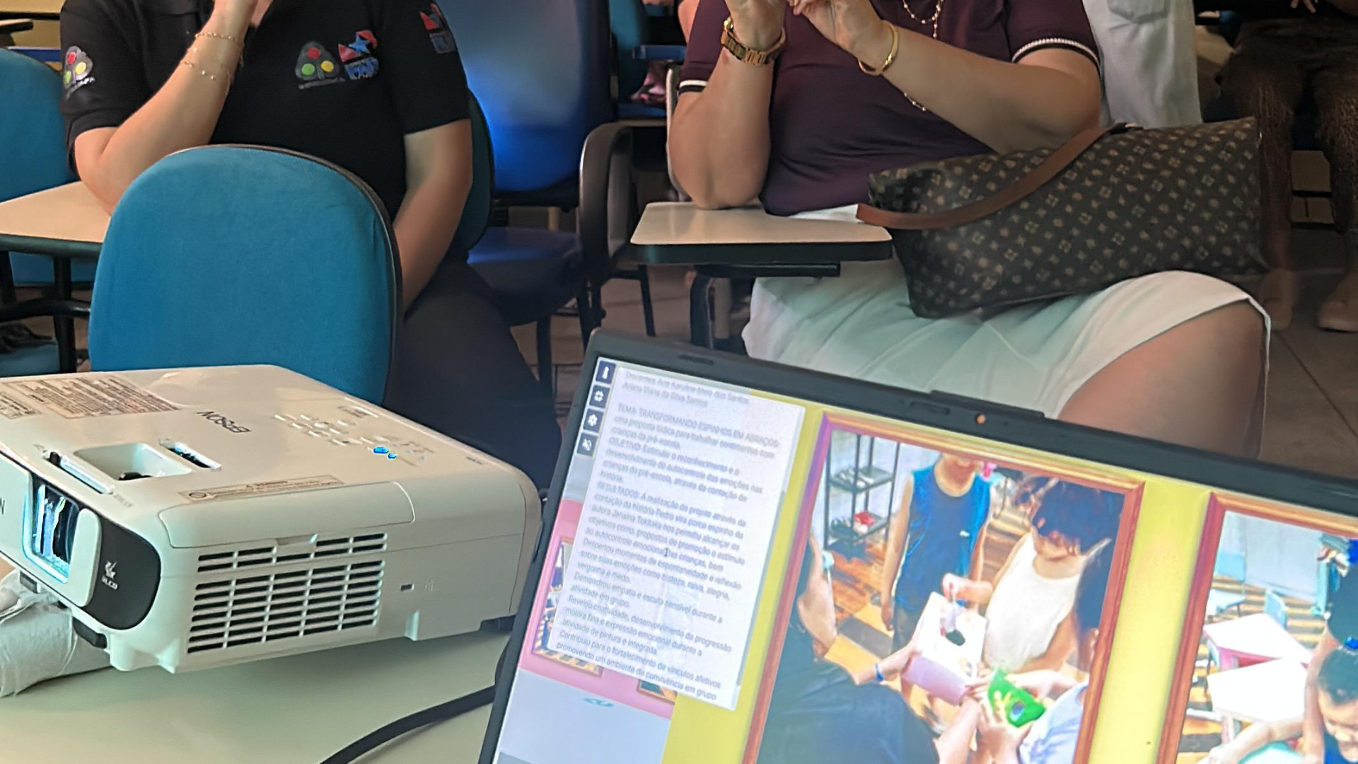 Participantes acompanham uma apresentação em sala de aula do Campus I da Uepa. Em primeiro plano, um projetor e um notebook exibem slides com conteúdos e registros fotográficos da atividade. Ao fundo, estudantes e servidores observam atentamente a exposição, sentados em cadeiras universitárias, durante um momento de formação e troca de conhecimentos.