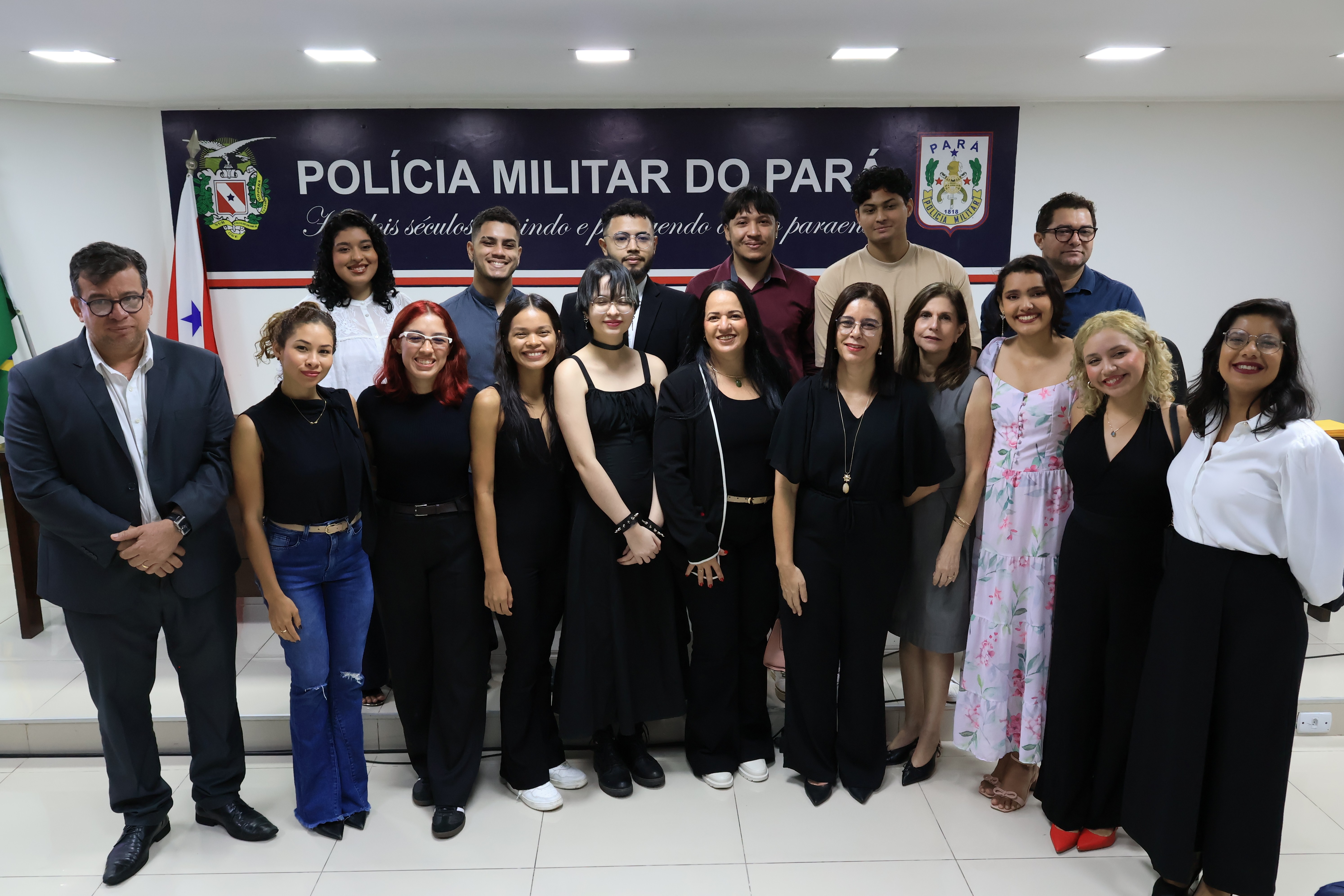A imagem mostra um grupo de pessoas posando para uma foto oficial em frente a um painel da Polícia Militar do Pará.  Os participantes estão vestidos de forma formal para a cerimônia de encerramento com entrega de certificados.