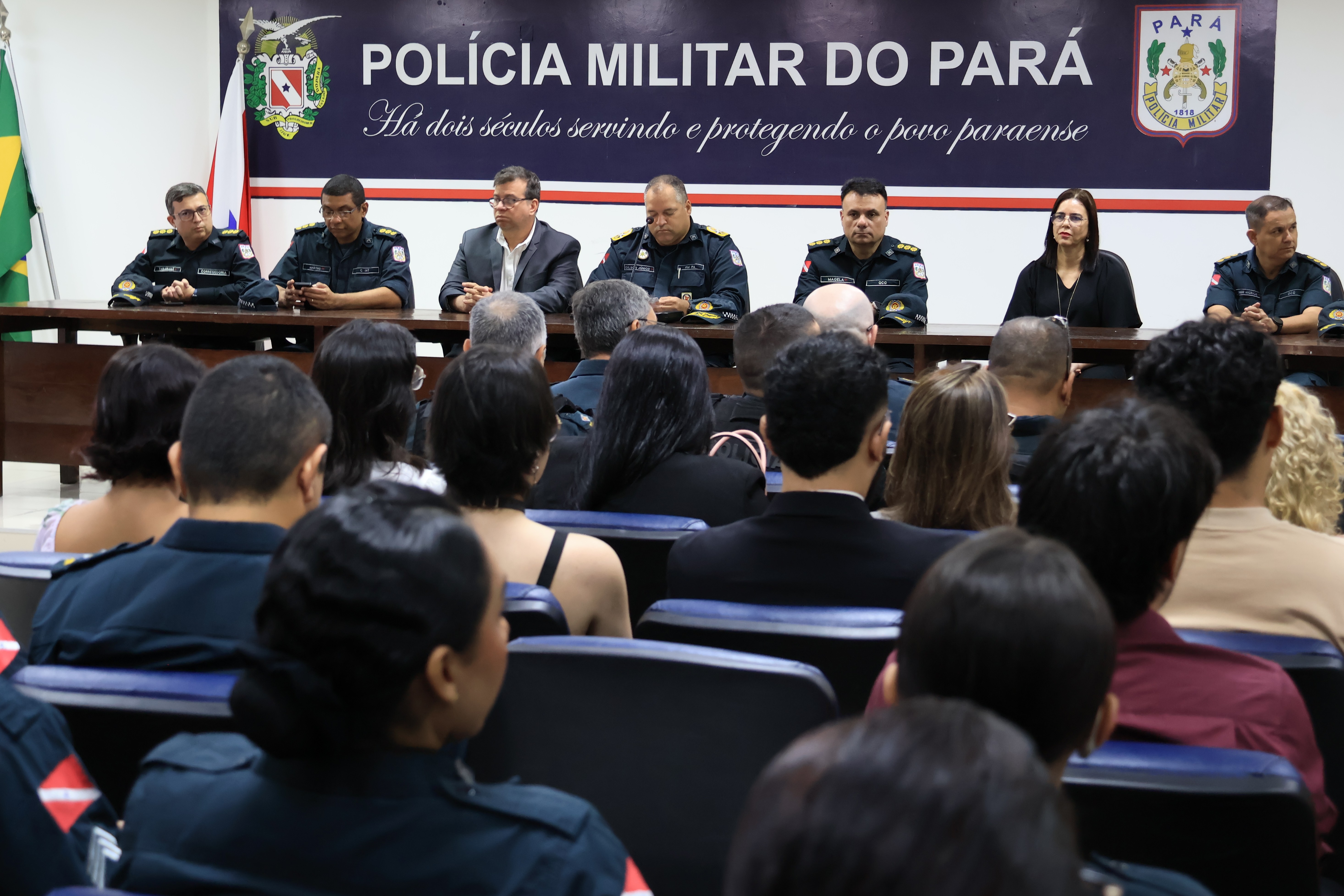 A imagem mostra uma cerimônia oficial da Polícia Militar do Pará, com uma mesa de autoridades composta por oficiais da corporação e convidados civis, posicionados à frente de um público atento.