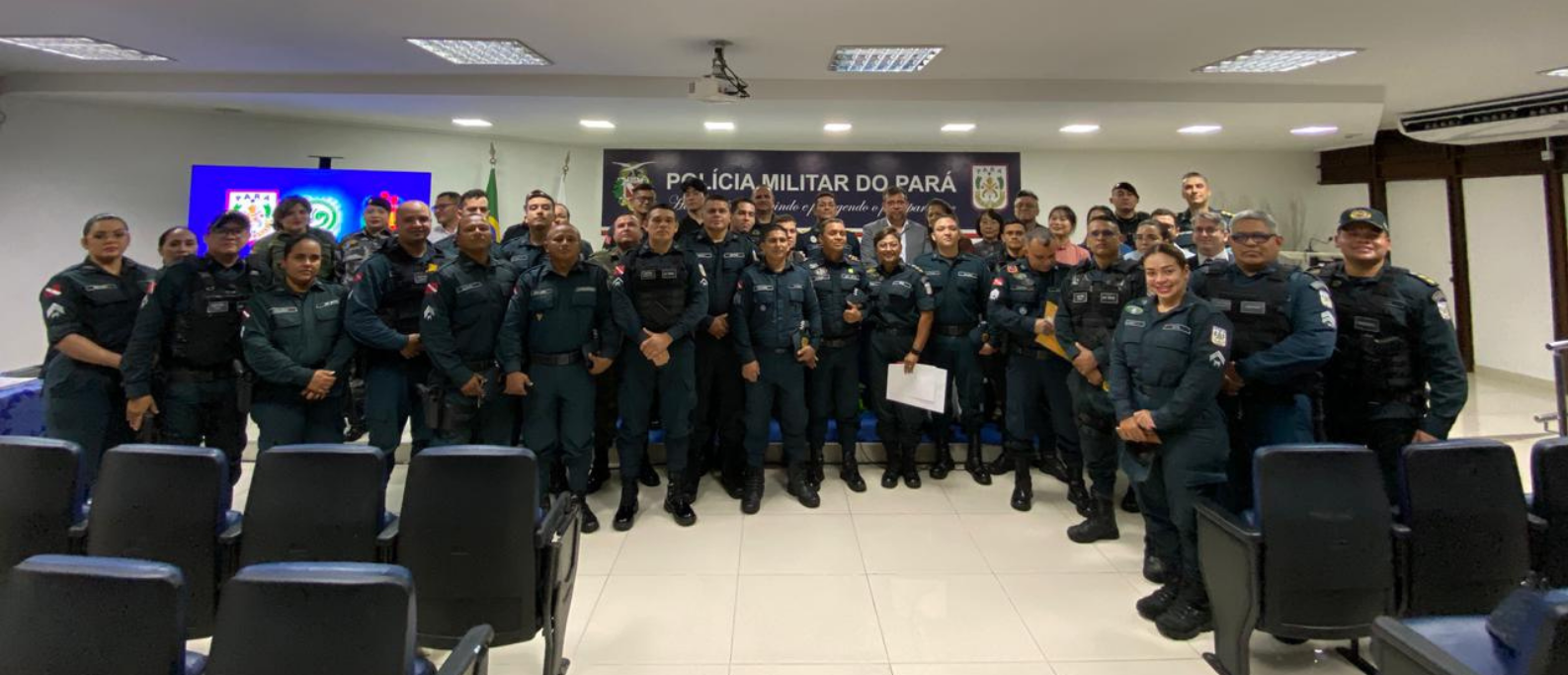 Grupo de policiais militares do Pará posa para uma foto oficial em auditório, após a cerimônia. Todos estão uniformizados e posicionados à frente do palco, sob o painel da Polícia Militar do Pará.