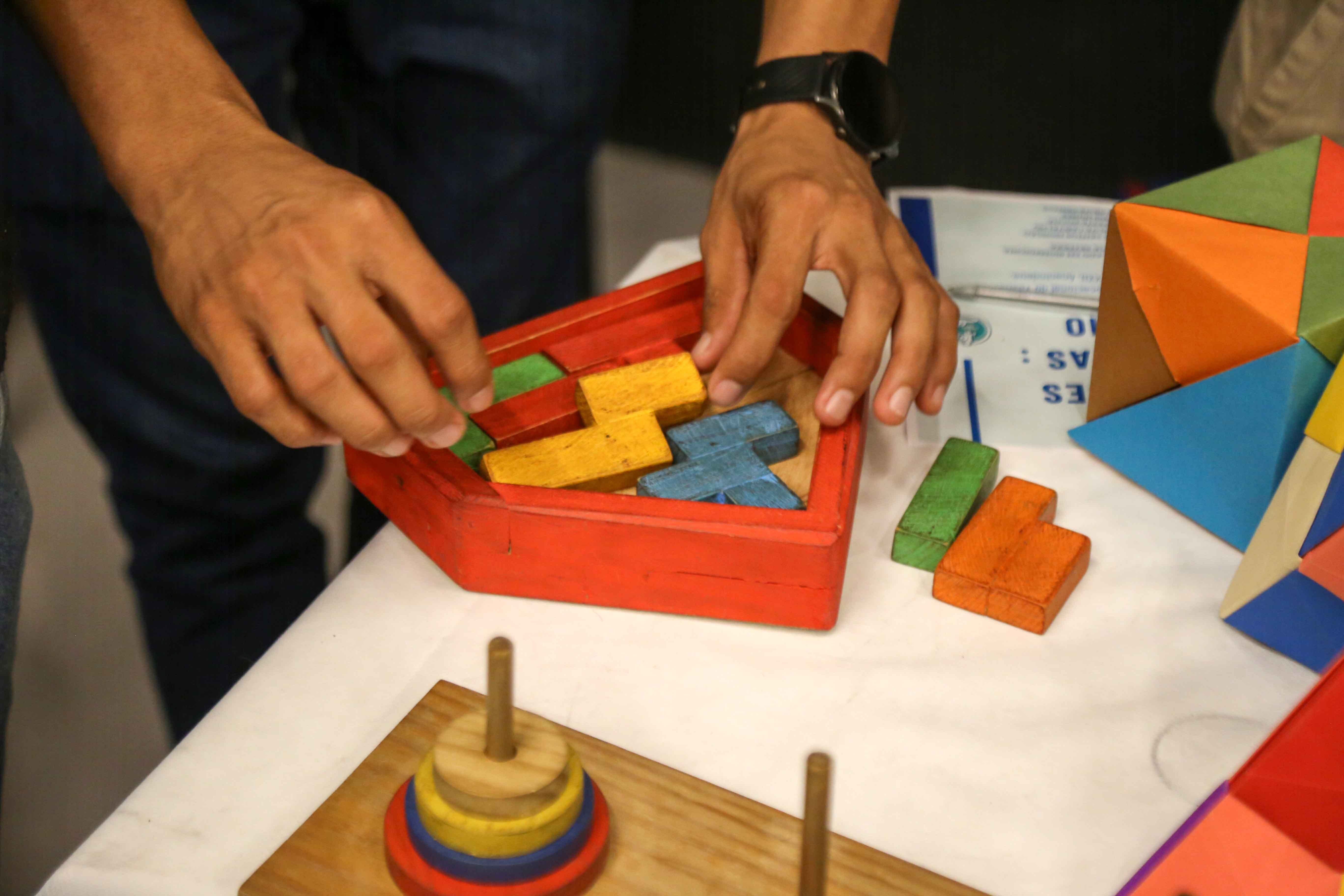 A imagem mostra mãos de uma pessoa manuseando um brinquedo de lógica matemática