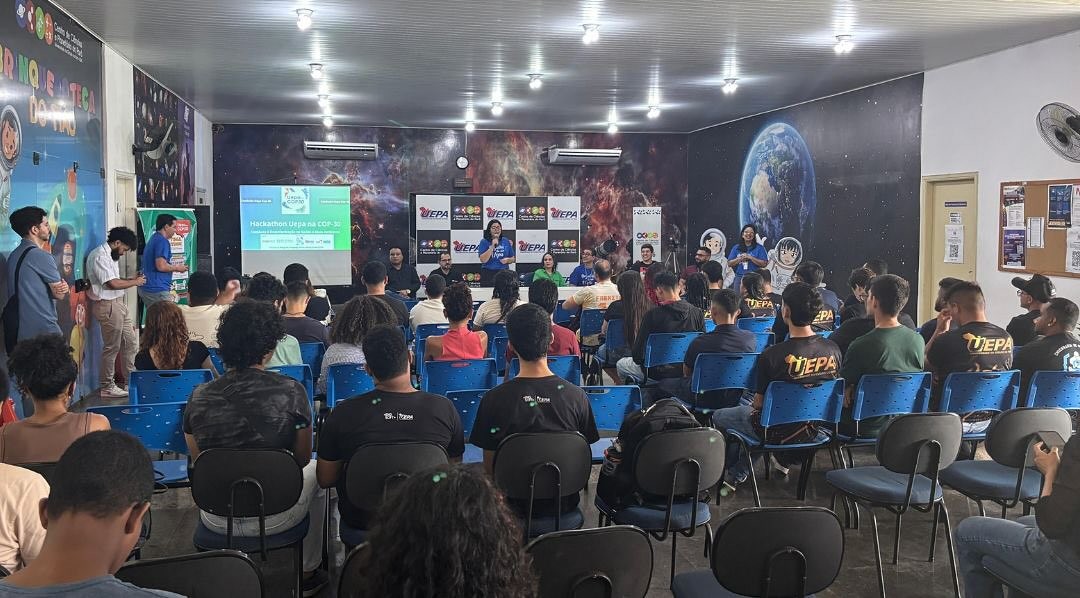 A imagem mostra um auditório cheio de estudantes e professores durante o lançamento da Maratona Hackathon Uepa na COP 30, realizado no Centro de Ciências e Planetário do Pará. No palco, representantes da organização apresentam informações sobre o evento, com telão e banners da Uepa ao fundo.