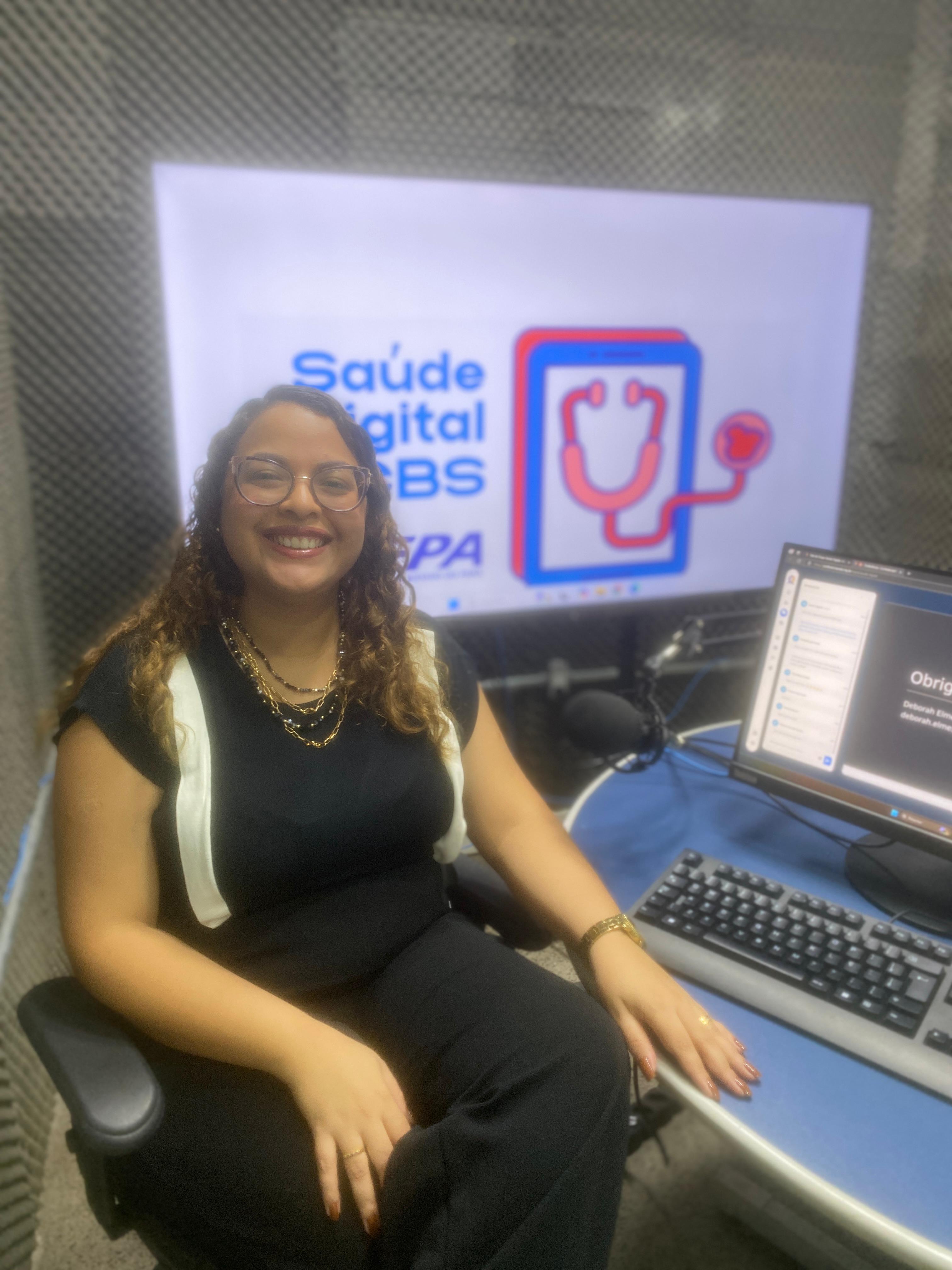 A imagem mostra uma pessoa em um estúdio sentada em frente de um computador e a tela exibe a logomarca do Saúde Digital