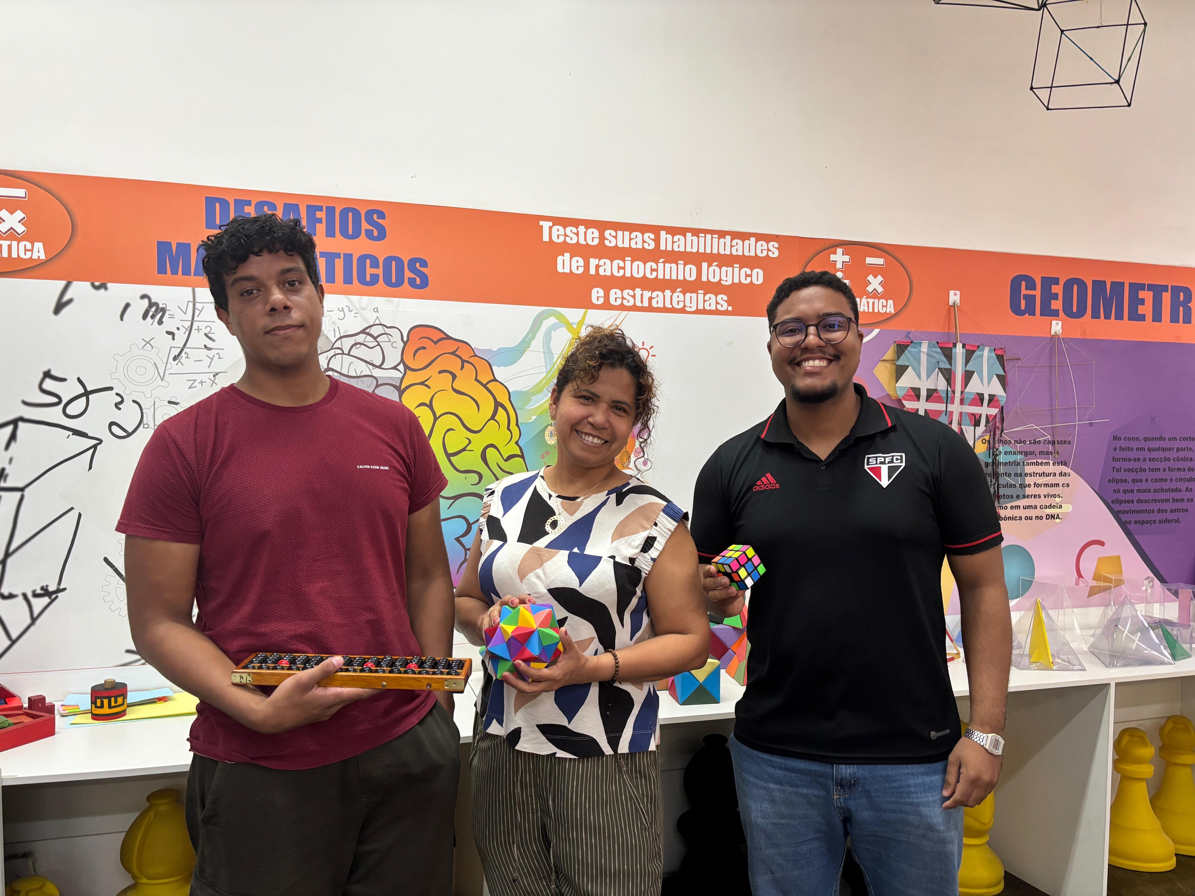 Na foto, parte da equipe que compõe a área da Matemática do Centro de Ciências e Planetário do Pará.  Ao fundo, há um mural colorido com as palavras “Desafios Matemáticos” e “Geometria”, além de ilustrações de cérebros, formas geométricas e fórmulas matemáticas.