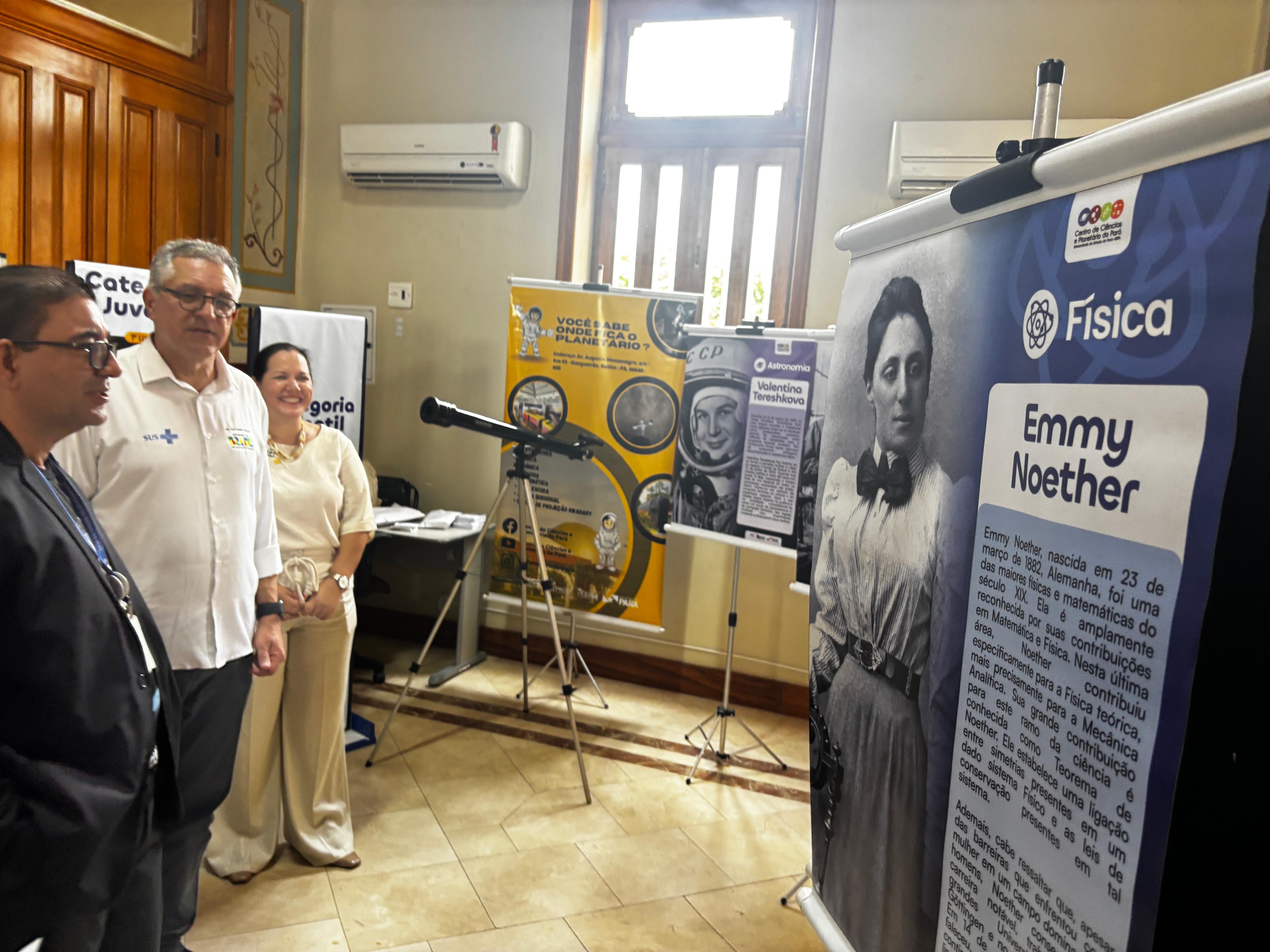 A foto mostra um grupo de três pessoas em pé: o diretor do CCPPA, José Roberto Silva, o ministro da Saúde, Alexandre Padilha, e a diretora do IEC, Lívia Martins. Eles se encontram dentro do museu do Instituto Evandro Chagas, na sala que abriga a exposição  “Constelações Femininas: Mulheres que Iluminam a Ciência”.