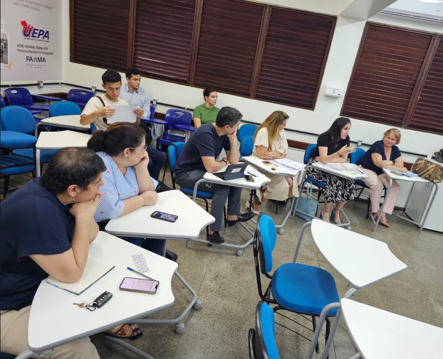 A imagem mostra pessoas sentadas em uma sala de aula ou reunião num ambiente acadêmico