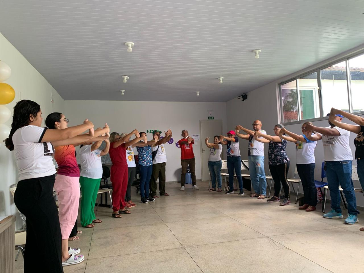 A imagem mostra um grupo de pessoas realizando um tipo de atividade ou exercício de ginástica laboral, em um ambiente institucional.