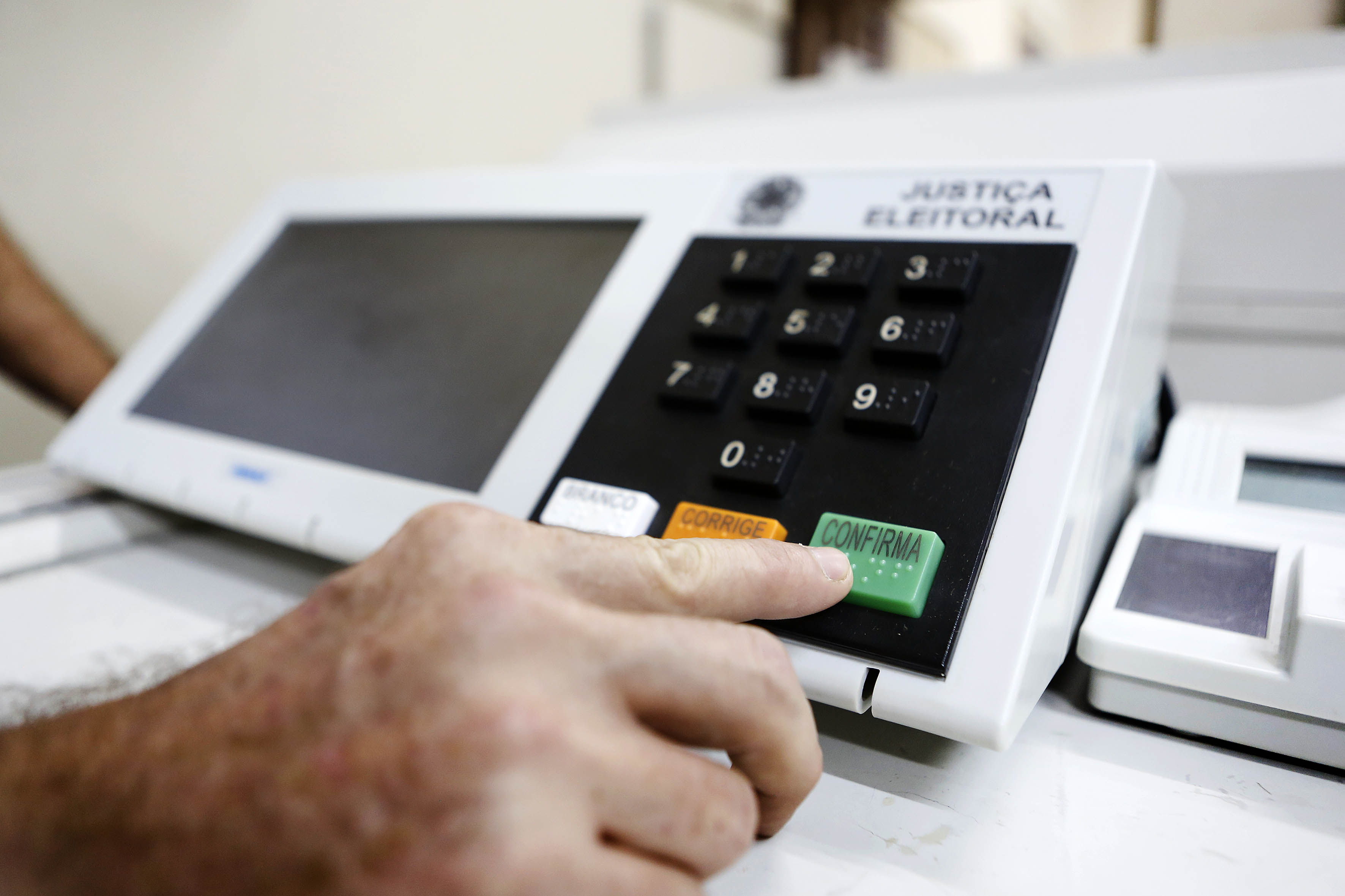 a imagem mostra uma urna eletrônica e alguém votando