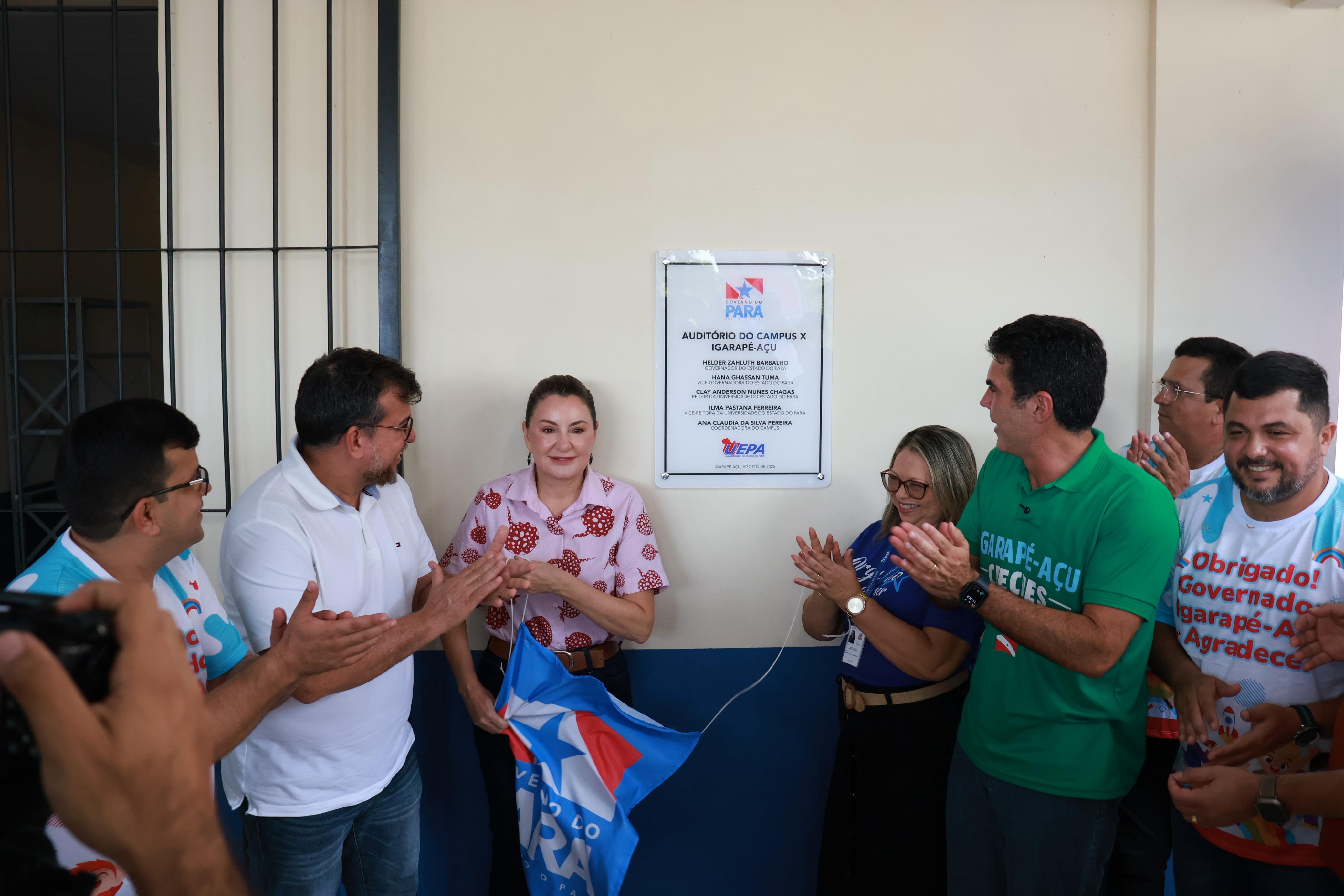 A imagem mostra um grupo de pessoas em frente à placa de inauguração do auditório do campus da Uepa em Igarapé-açú. Todos aplaudem e celebram o momento.