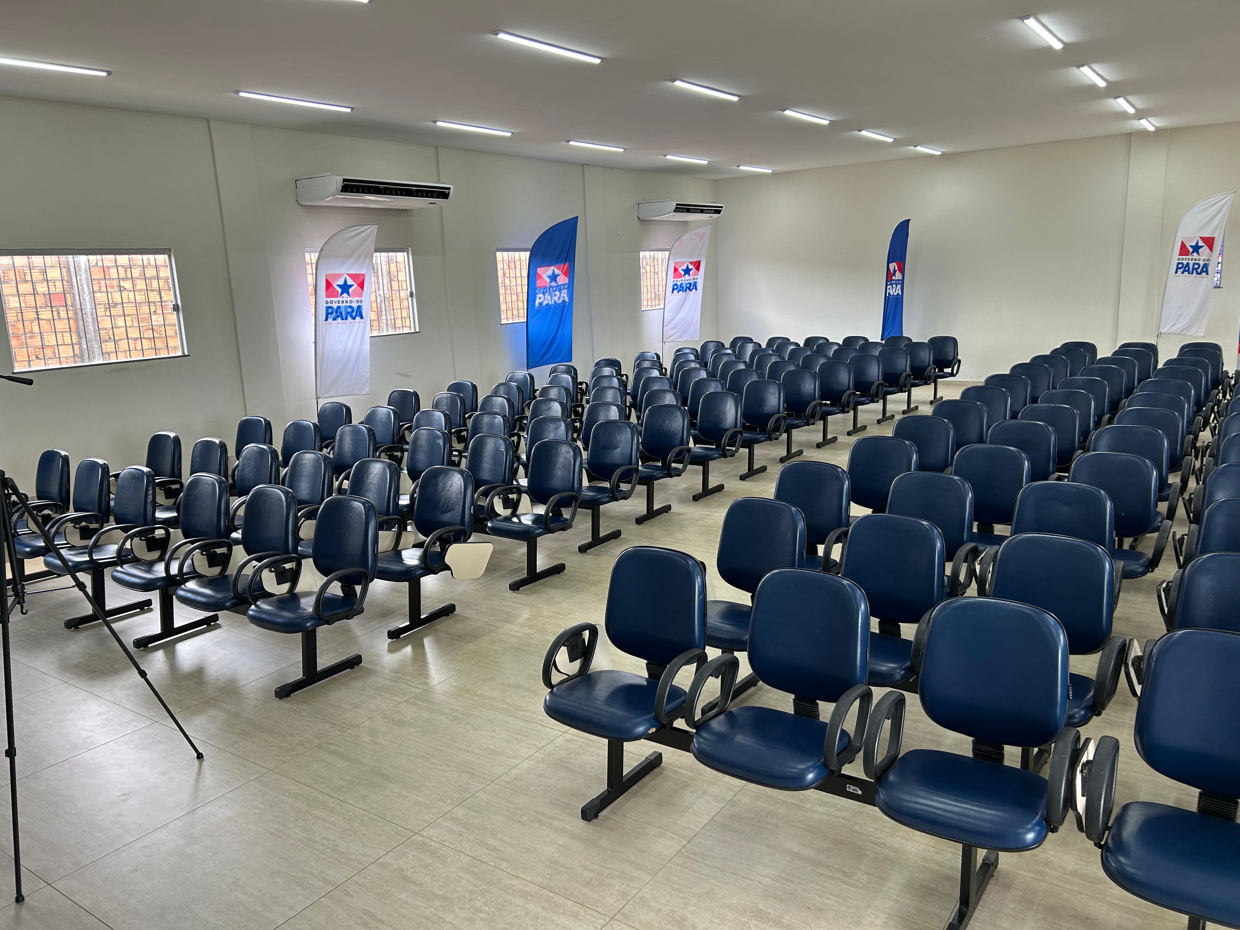 A imagem mostra um auditório amplo e moderno com várias fileiras de cadeiras. 