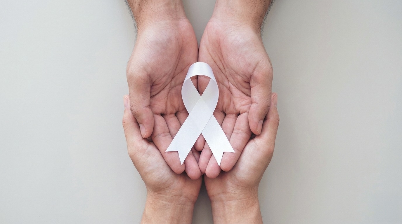 A imagem mostra duas mãos abertas e unidas em forma de concha, segurando um laço branco. O fundo é neutro e claro.