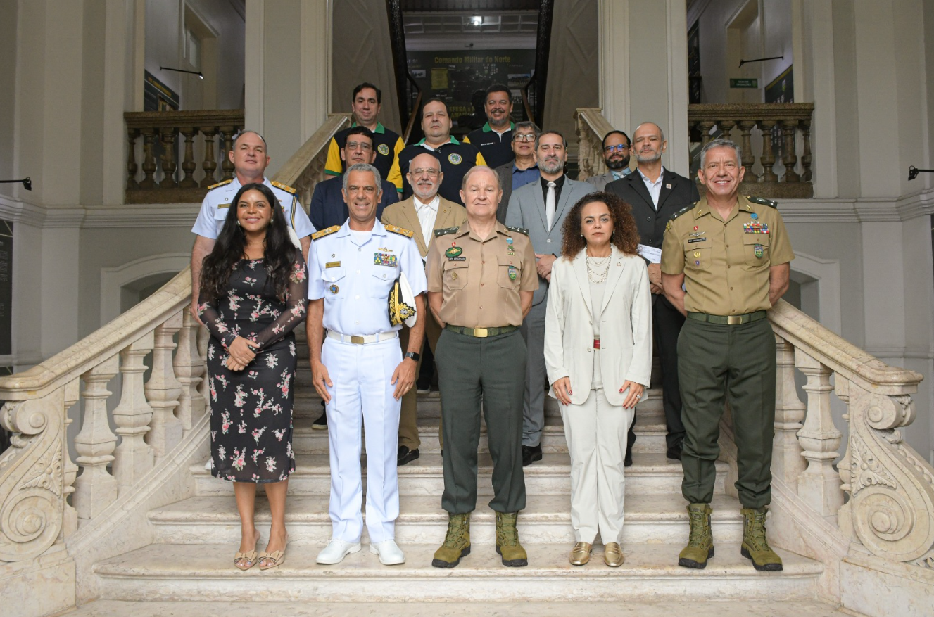  Um grupo de pessoas posa para uma foto oficial em uma escadaria interna de um edifício histórico. Entre os presentes, há militares do Exército, Marinha e Aeronáutica, além de civis em trajes formais. O ambiente tem arquitetura clássica com corrimões ornamentados.