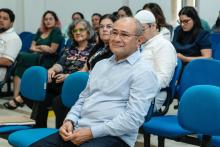 Público sentado no auditório, com destaque para um senhor sorridente em primeiro plano.